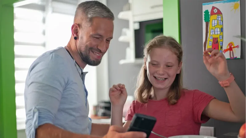 Zwei Personen schauen auf ein Smartphone und freuen sich.